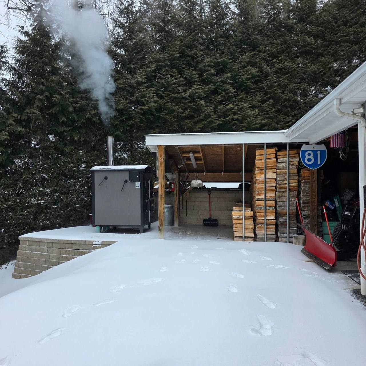 A HeatMaster outdoor boiler near a house and woodshed in the snow