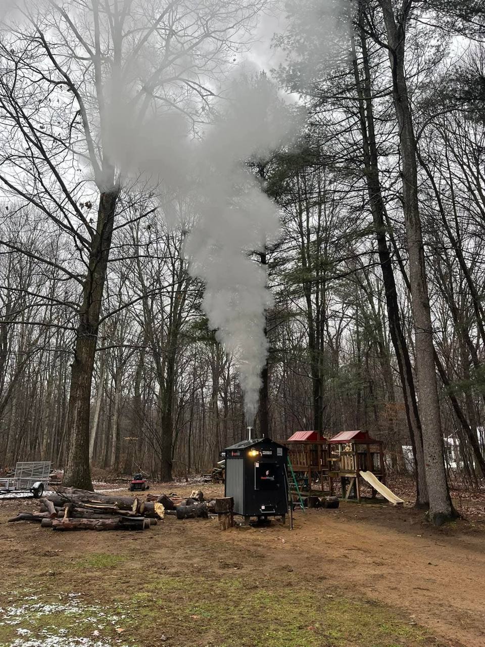 An outdoor wood boiler sending up a big plume of smoke in the woods
